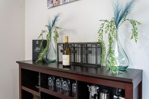 Eine Bar mit Weinflasche, Gläsern und dekorativen Pflanzen auf einem Holzregal.
