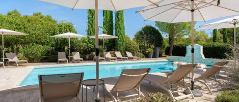 Un área junto a la piscina con sillones de descanso y sombrillas.
