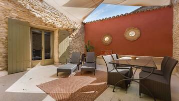 Une terrasse avec des meubles en osier, une table en verre et un mur en pierre.