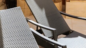 Patiolla on kaksi aurinkotuolia, pieni pöytä, kaktus, ruukussa oleva kasvi ja tyynyillä varustettu sohva.