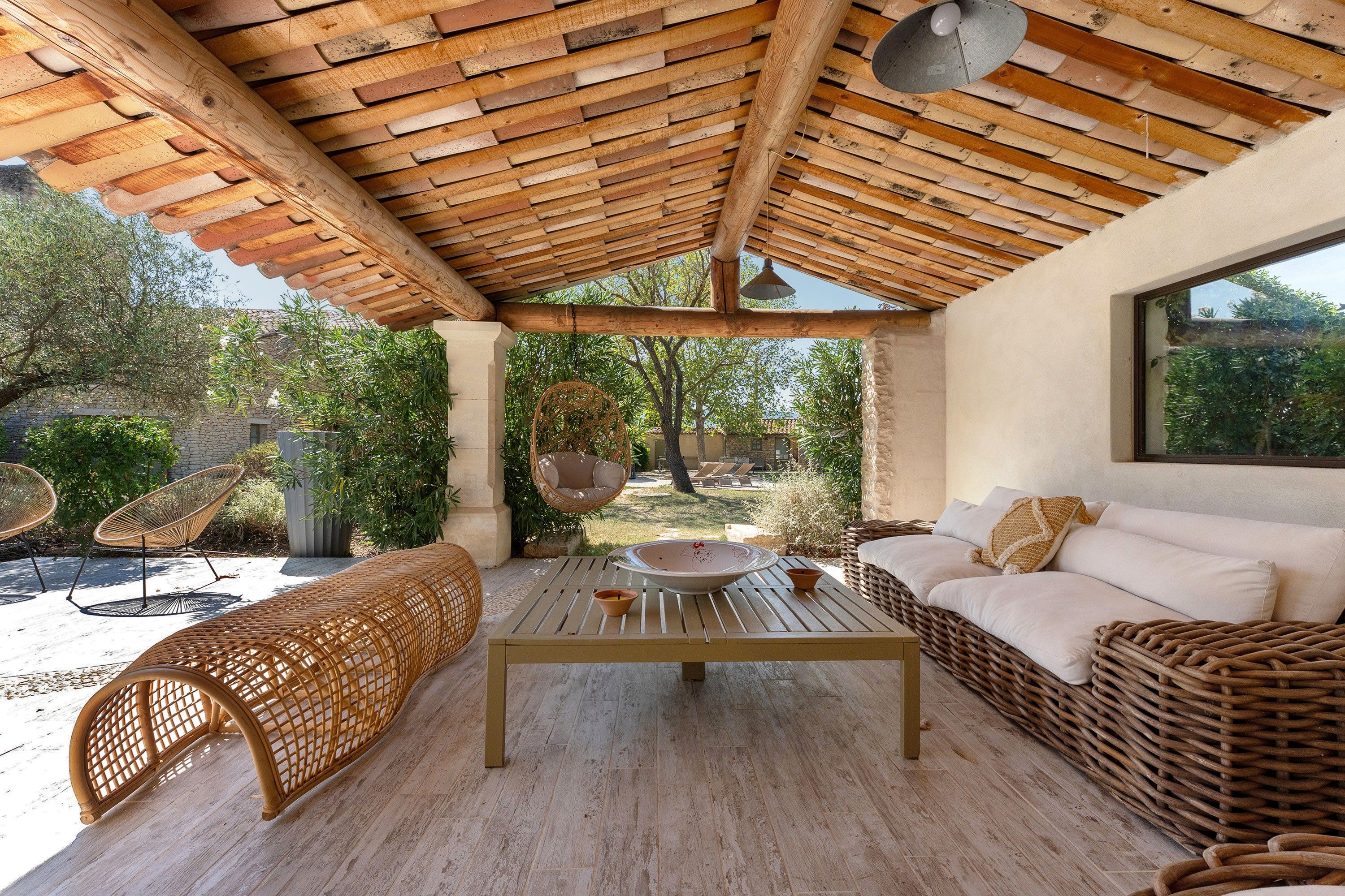 Een overdekt terras met houten afwerking, rieten meubels en uitzicht op de tuin.