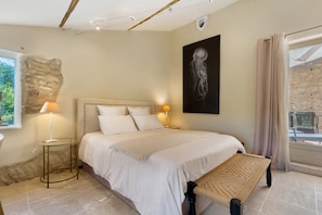 A bedroom with a bed, two bedside lamps, a wall-mounted artwork, and a window with curtains. - Olivier Apartment with Pool, Mountain View, Wi-Fi, and Air Conditioning (Cabrières-d'Avignon)