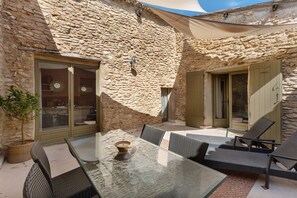 A stone building with a glass table and wicker chairs, a potted plant, and a door. - Olivier Apartment with Pool, Mountain View, Wi-Fi, and Air Conditioning (Cabrières-d'Avignon)