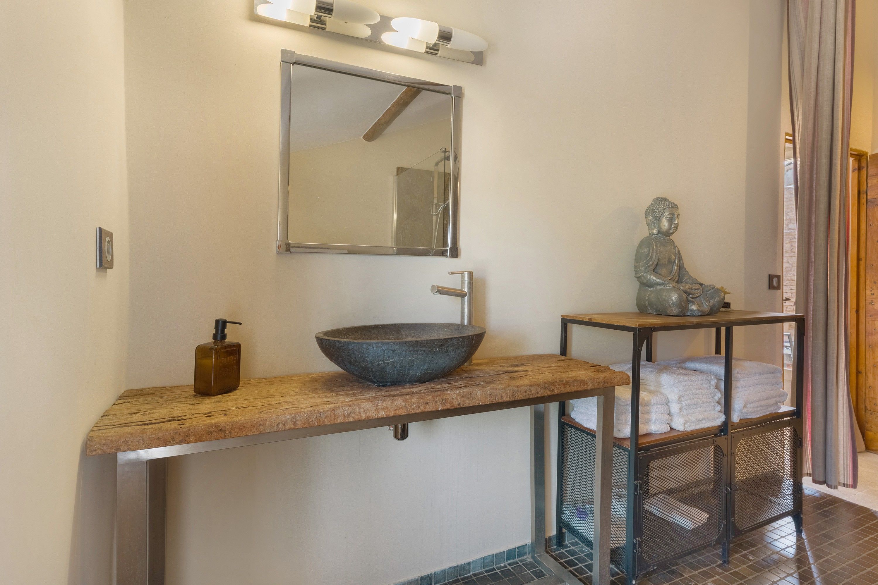 A bathroom with a large vessel sink, a mirror, a Buddha statue, and a towel rack.