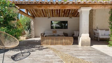 Un espace extérieur abrité, aménagé avec un banc en osier tressé, une chaise en rotin et un pilier en pierre.