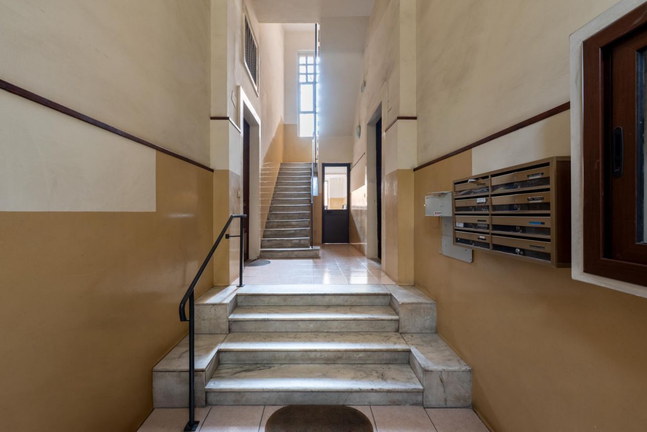 Un escalier menant à l’étage supérieur, avec une rampe, une porte en haut et une fenêtre laissant entrer la lumière naturelle.