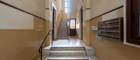 A staircase leading to an upper floor with a handrail, a door at the top, and a window providing natural light.