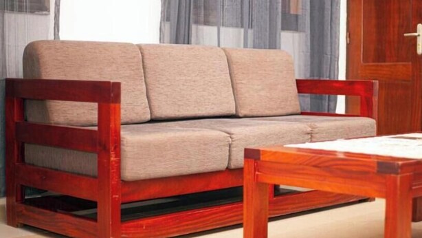 Un sofá de madera con un cojín, una mesa de centro a juego de madera y una puerta de madera al fondo.