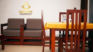 A room with two wooden chairs, a dining table with a yellow tablecloth, and a logo on the wall.