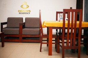 A room with two wooden chairs, a dining table with a yellow tablecloth, and a logo on the wall.