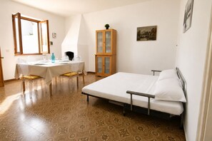 Ein Schlafzimmer mit einem Bett, einem Esstisch mit Stühlen, einem Schrank und einem Fenster.