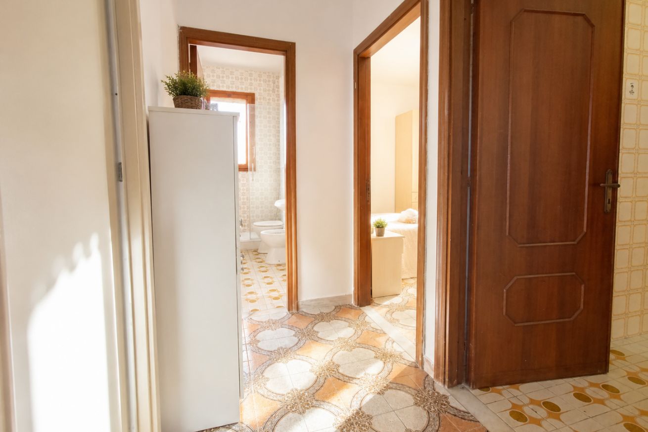 A hallway with a refrigerator, a wooden door, and patterned flooring leading to a bathroom.