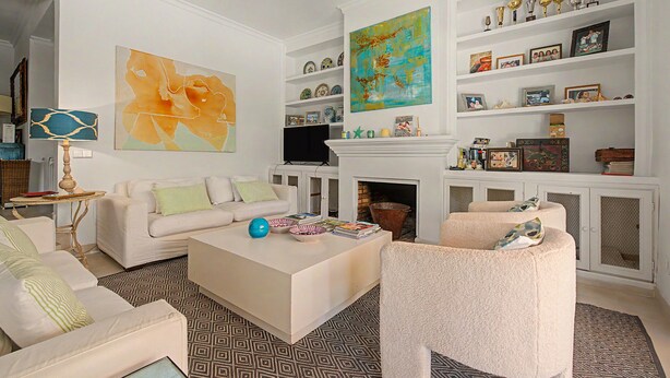 A living room with a white sofa, a coffee table, and a fireplace. There are shelves with decorative items and a large abstract painting. - Stunning private villa in Sotogrande (Zone C) with garden, private pool, and Wi-Fi (San Roque)