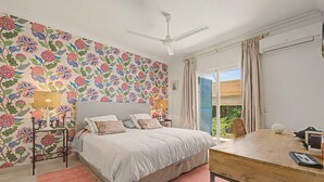 A bedroom with a bed, a bedside table, a ceiling fan, a window with curtains, and a view of greenery outside. - Stunning private villa in Sotogrande (Zone C) with garden, private pool, and Wi-Fi (San Roque)