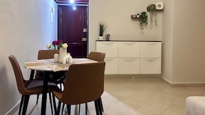 Ruokailutila, jossa on neljälle katettu pöytä, pöydän ympärillä tuoleja, maljakko kukkineen ja kaappi koriste-esineitä varten.