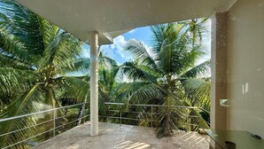 A balcony with a view of palm trees, a glass table, and a metal railing. - The Hilltop Boosa (Boossa)