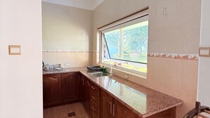 A kitchen with a window, cabinets, and a trash bin. - The Hilltop Boosa (Boossa)