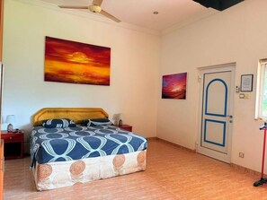 A bedroom with a bed, a nightstand, a door, and two wall-mounted paintings.