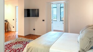 A bedroom with a bed, a television mounted on the wall, a door leading to a balcony, and a patterned rug on the floor.