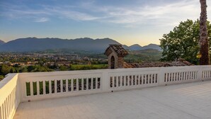 A balcony with a white railing overlooking a town and mountains.