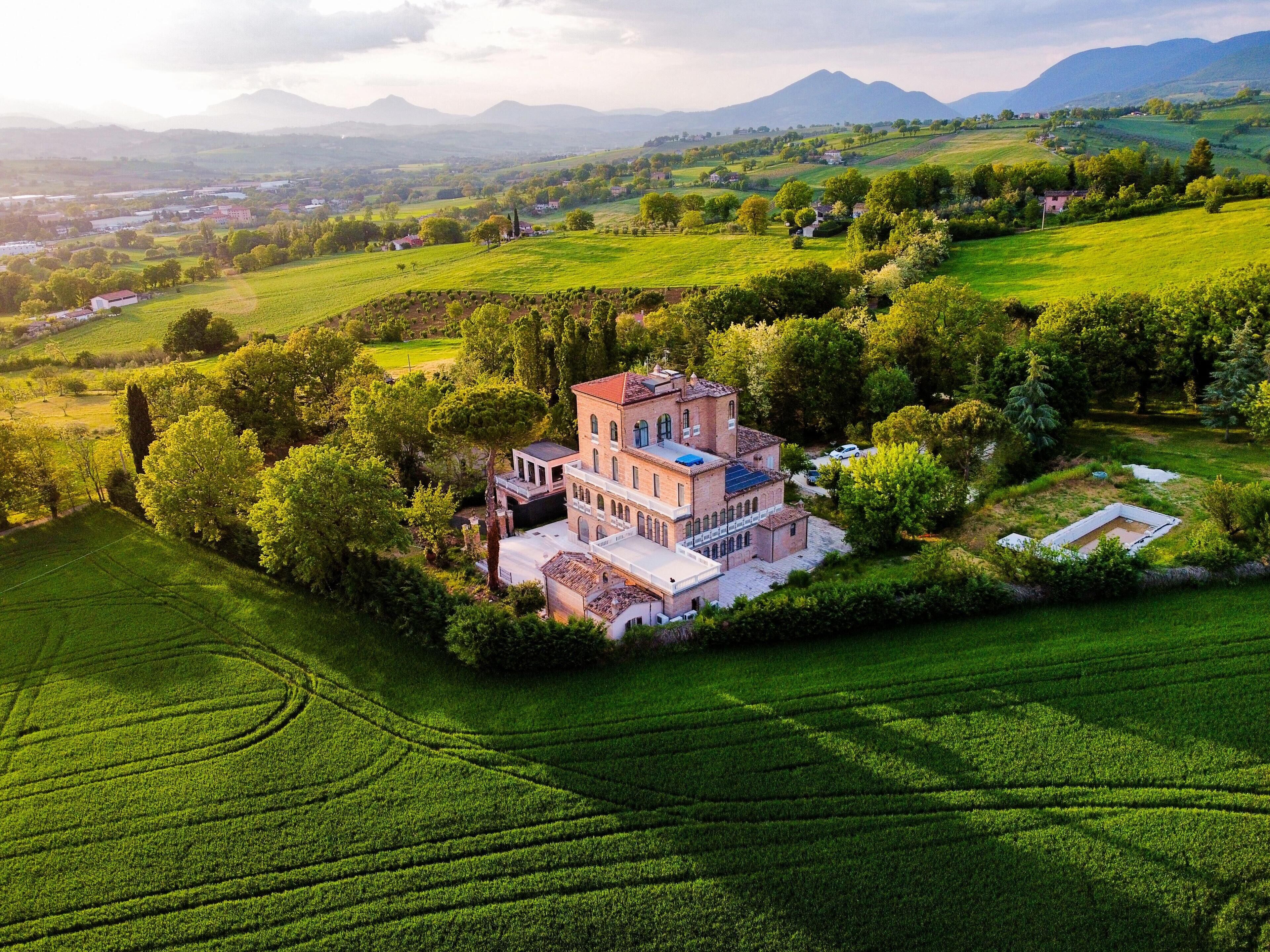 A large estate with a prominent building surrounded by lush greenery and fields.