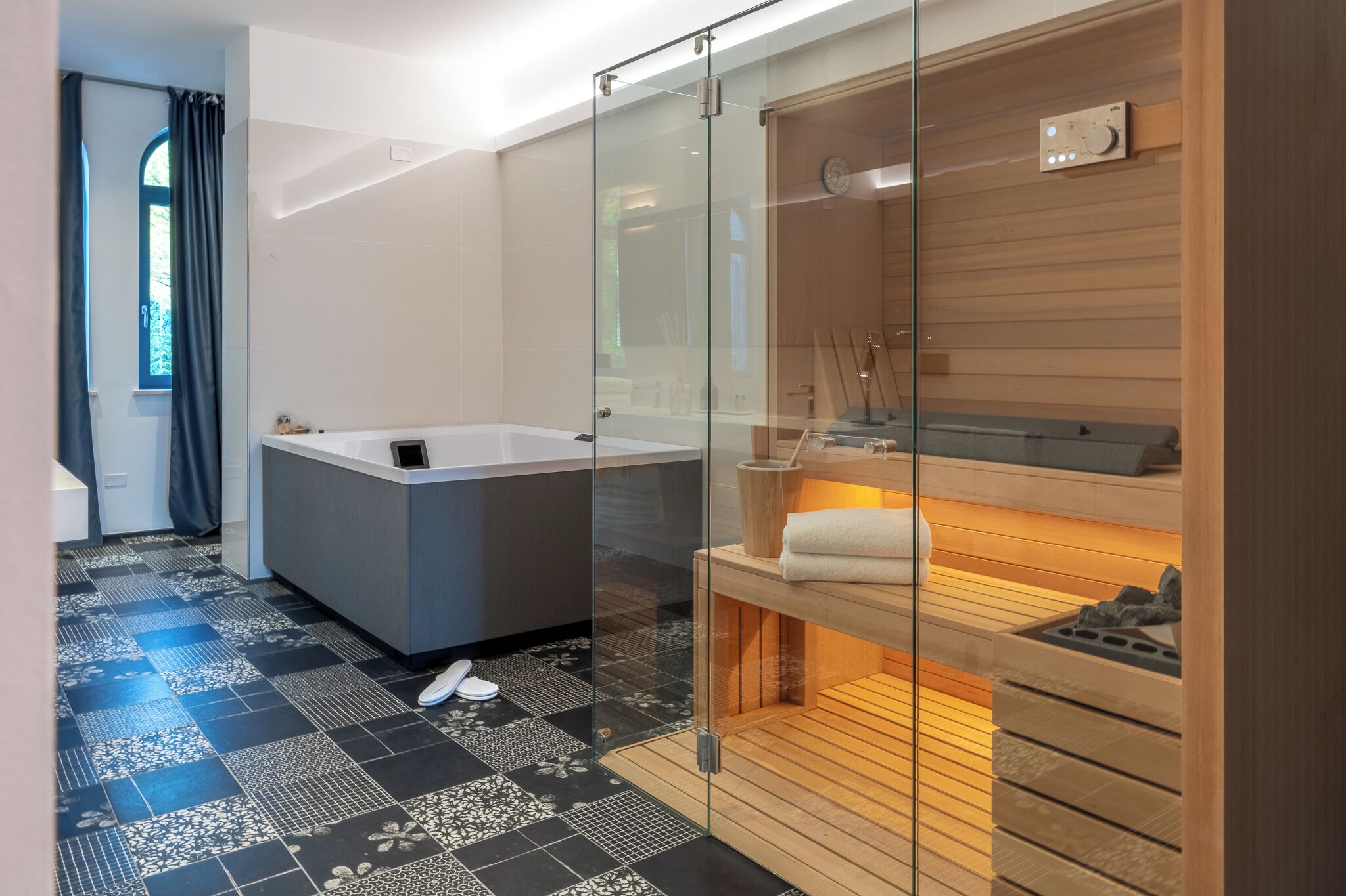 Un baño moderno con ducha envuelta en vidrio, bañera y banco de sauna de madera.