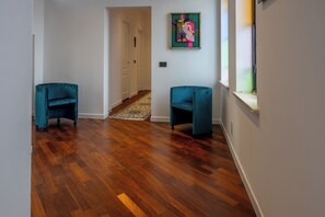 A hallway with wooden flooring, two teal chairs, a door, and a painting on the wall. - RELAIS FLORA BERTA (Matelica)