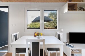A dining area with a white table, four chairs, a vase with flowers, and a TV on a stand.