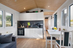 A modern kitchen with white cabinets, a black oven, and a wooden ceiling. - Tiny Home 'Haus Barsch' with Lake View, Wi-Fi and Air Conditioning (Lohmen)