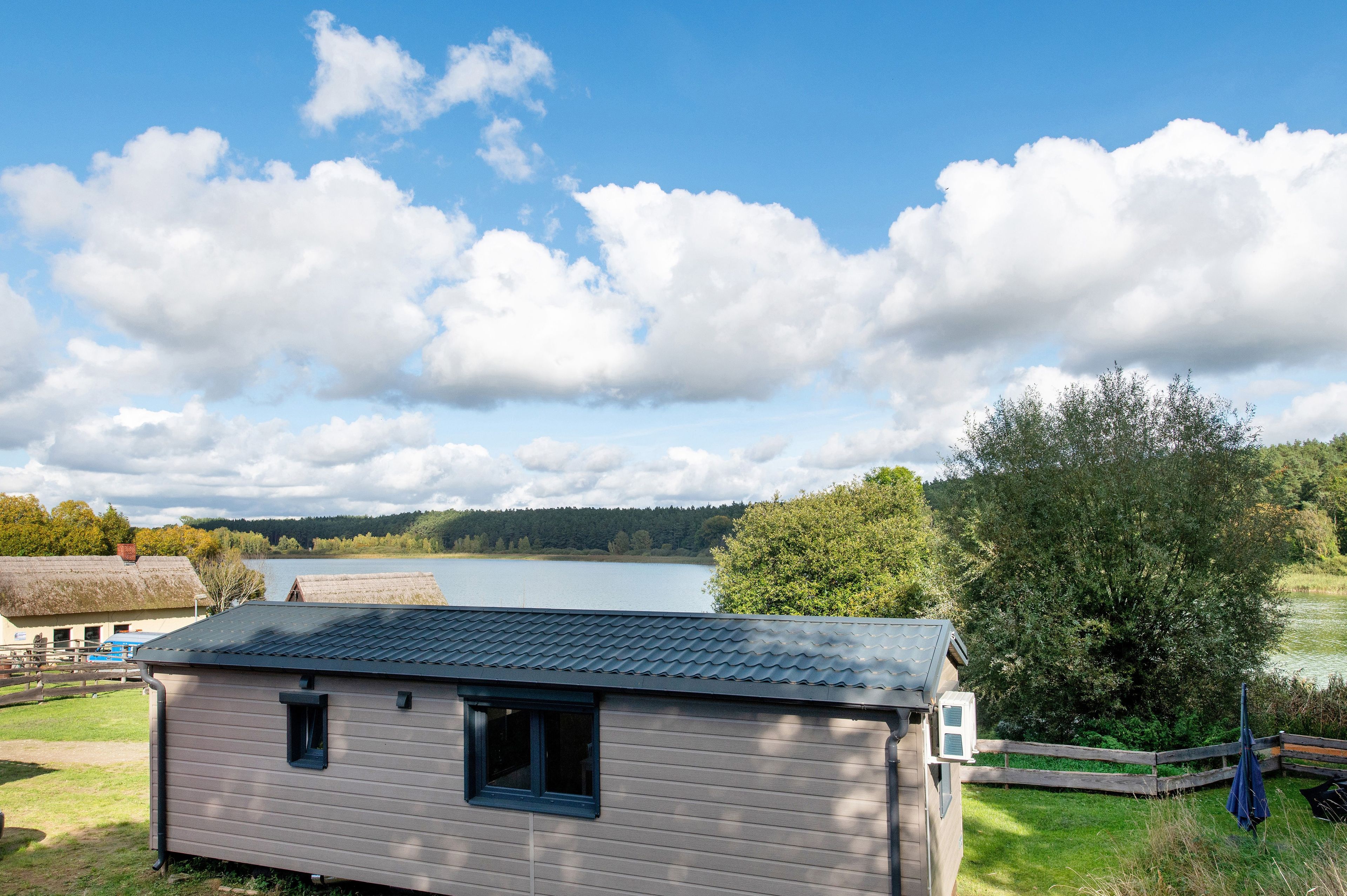 Eine kleine Holzhütte mit einem Reetdach, einem Fenster und Blick auf See und Wald.