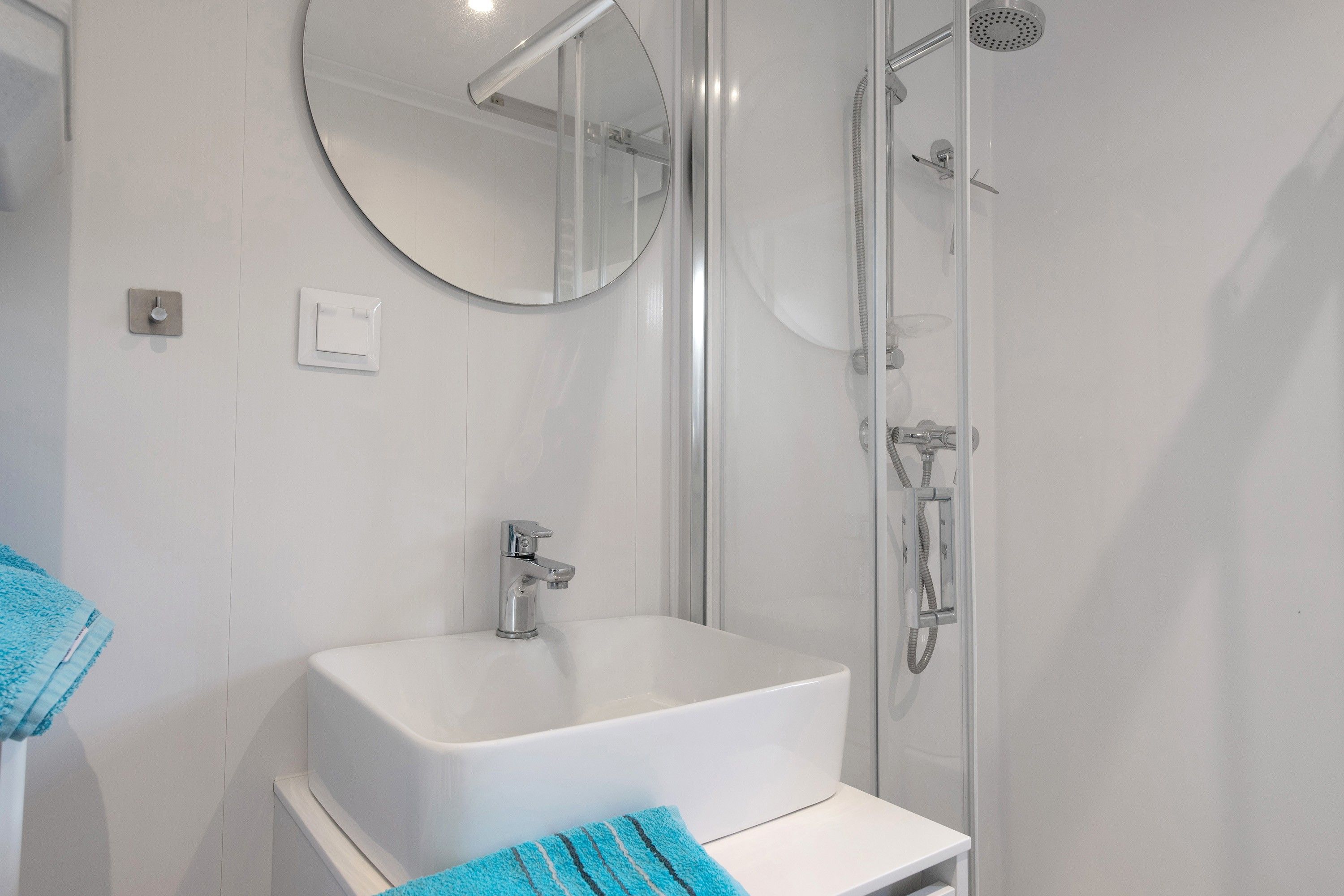Ein modernes Badezimmer mit einem weißen Waschbecken, einem Spiegel und einer Duschkabine.