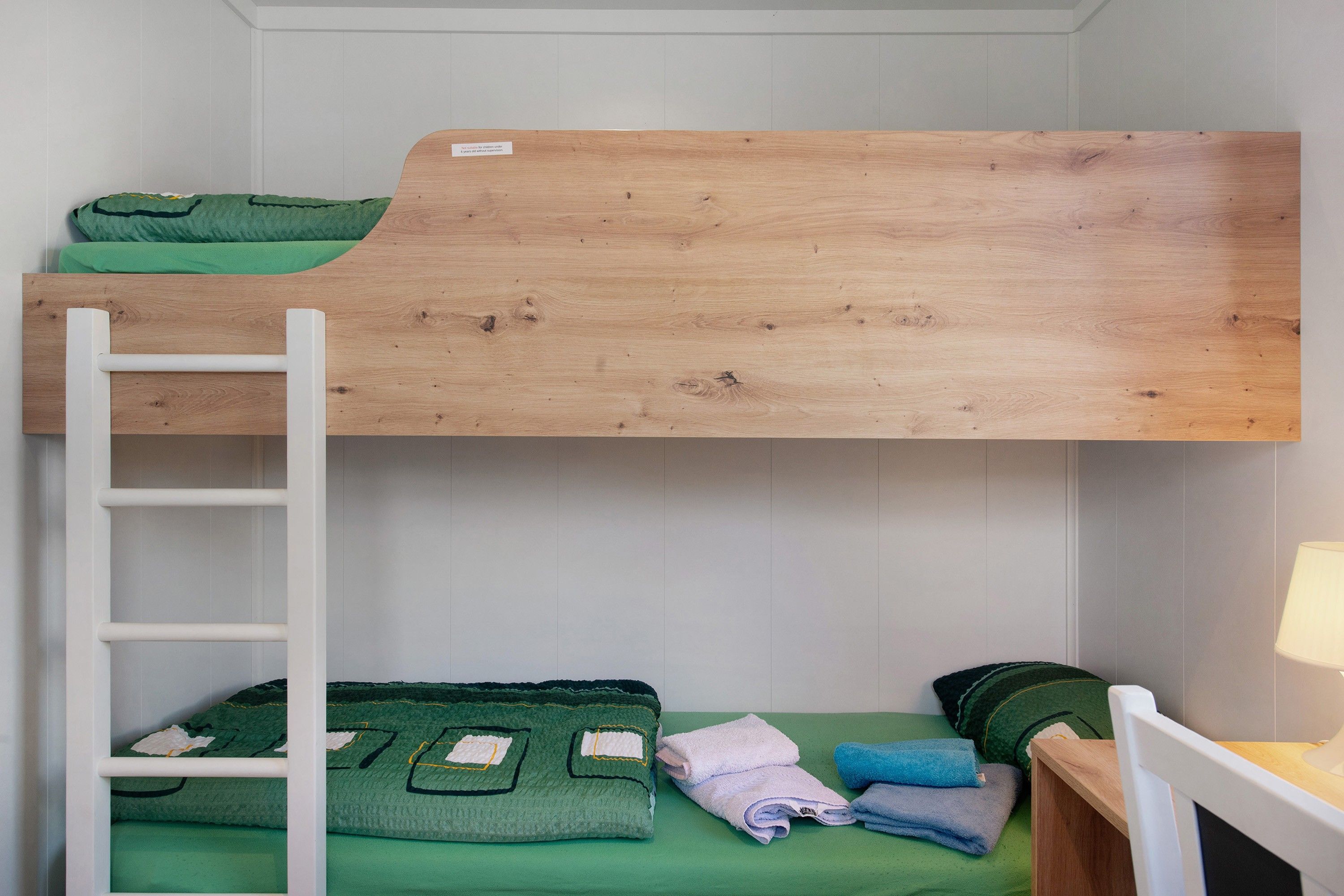 Ein Stockbett mit Holzkopfstück, einer Stehleiter und einem grünen, gesteppten Matratze.