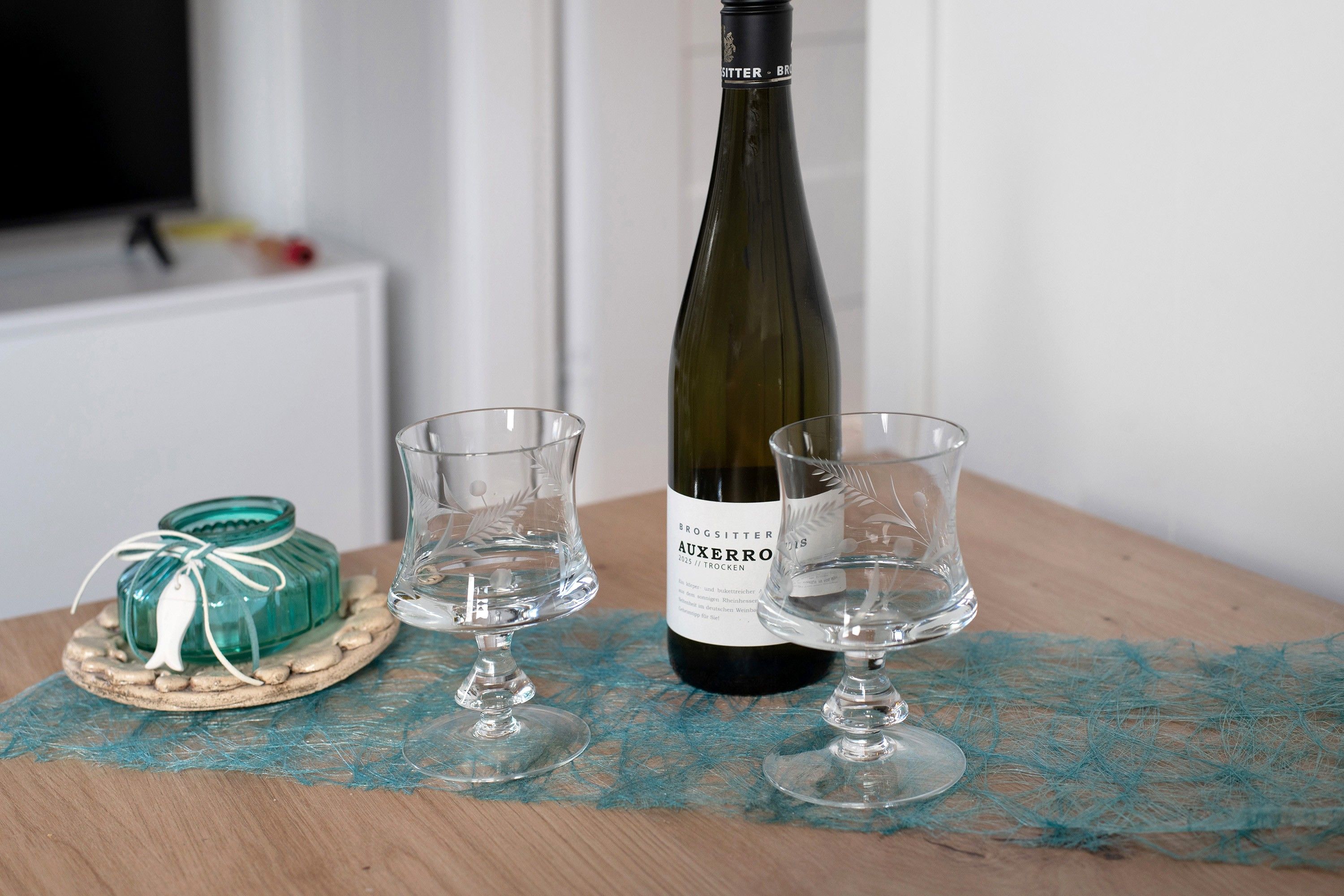 Een fles wijn en twee glaasjes op een tafel met een blauwe tafelloper van kant.