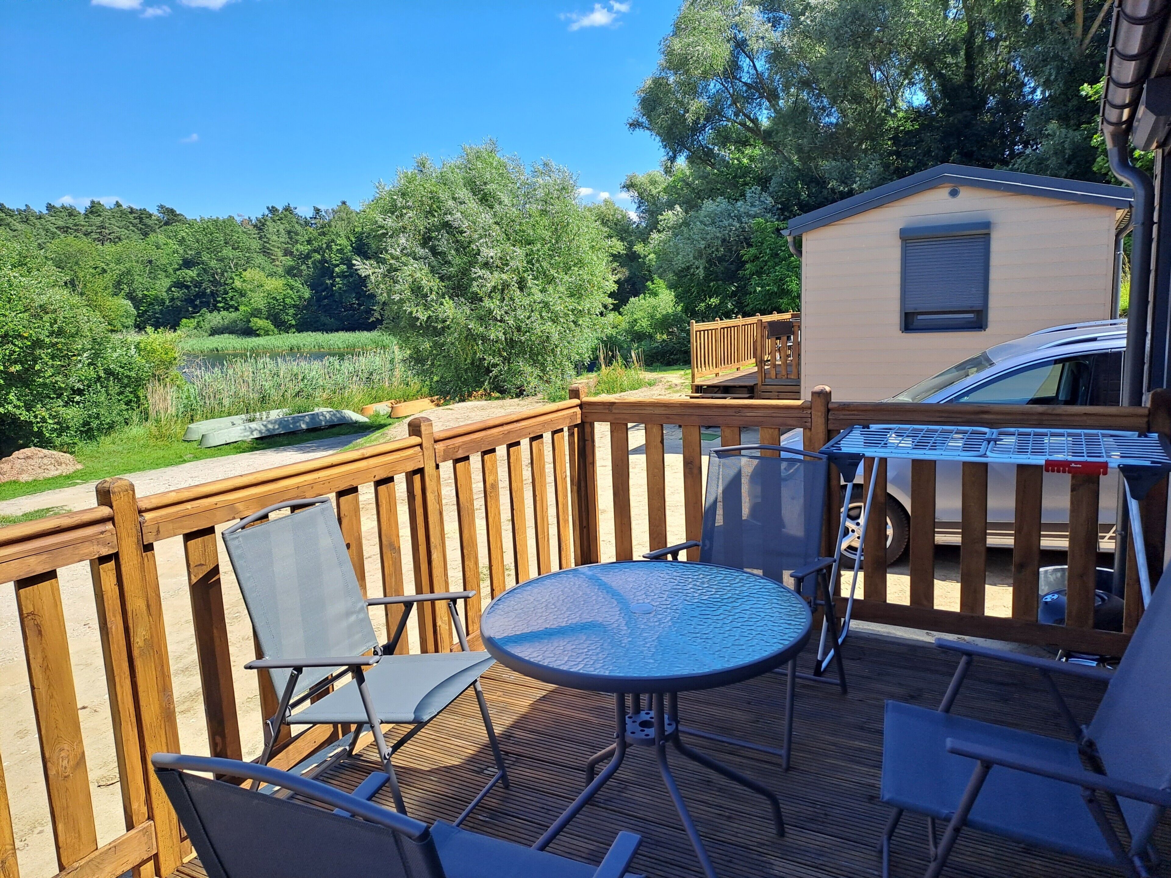 A wooden deck with a metal table and chairs, a small building, and a car parked nearby.