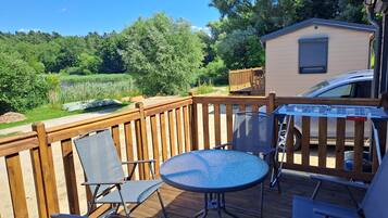 A wooden deck with a metal table and chairs, a small building, and a car parked nearby.