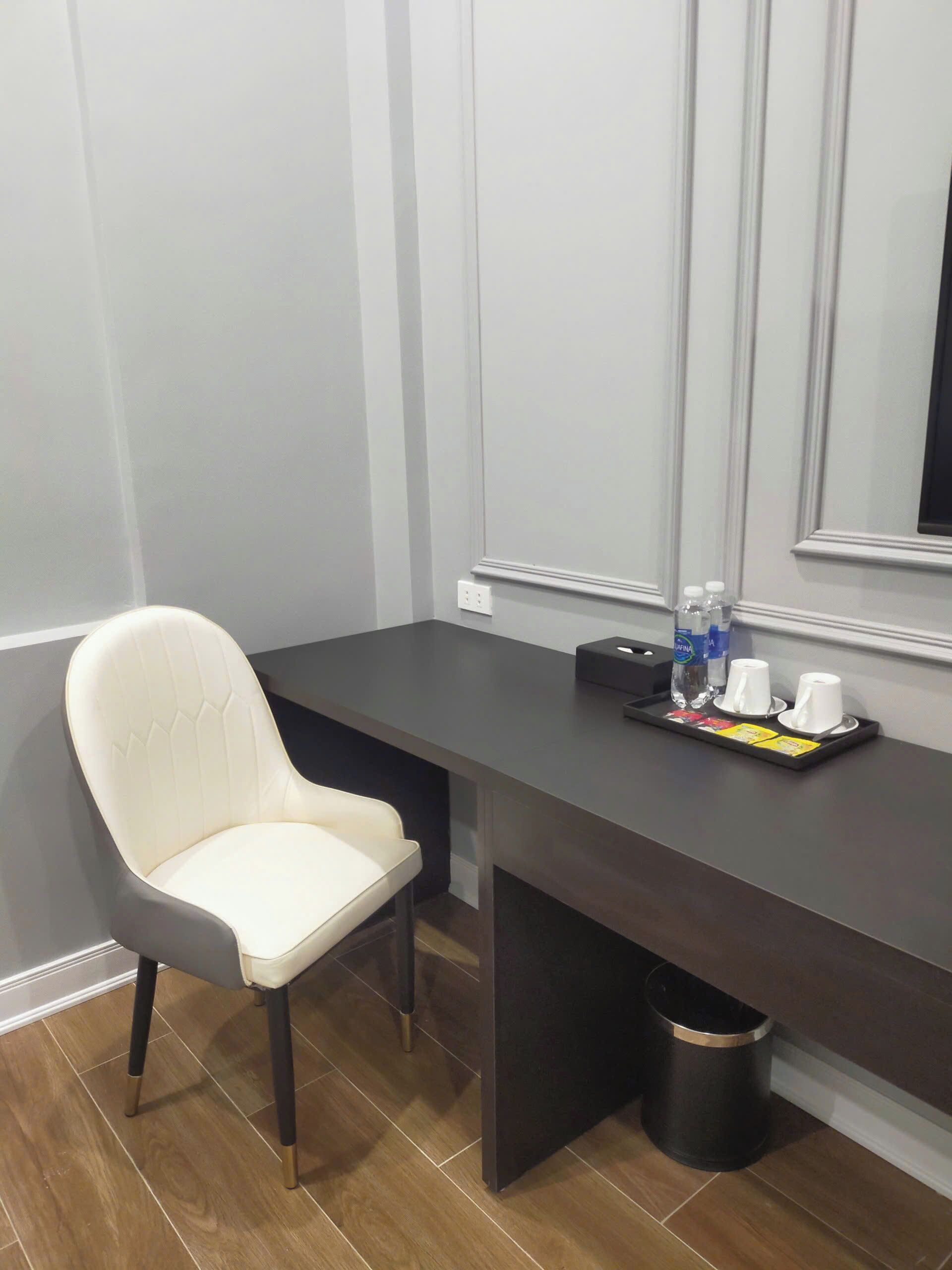 A modern room with a dark wooden desk, a white chair, and a trash bin.