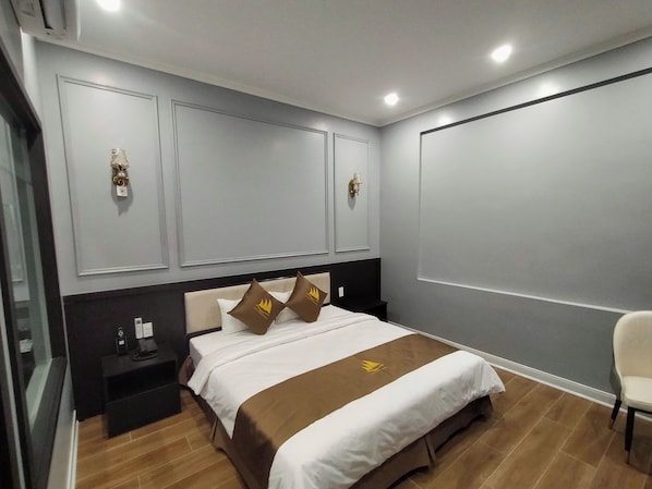 Una habitación de hotel con cama, mesitas de noche, una silla y un ventanal grande.