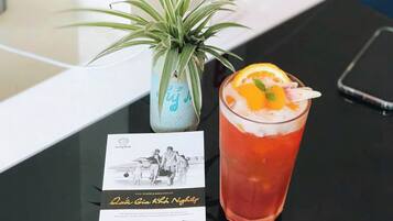 A glass of red beverage with an orange slice garnish on a black table, a small potted plant, and a printed menu.