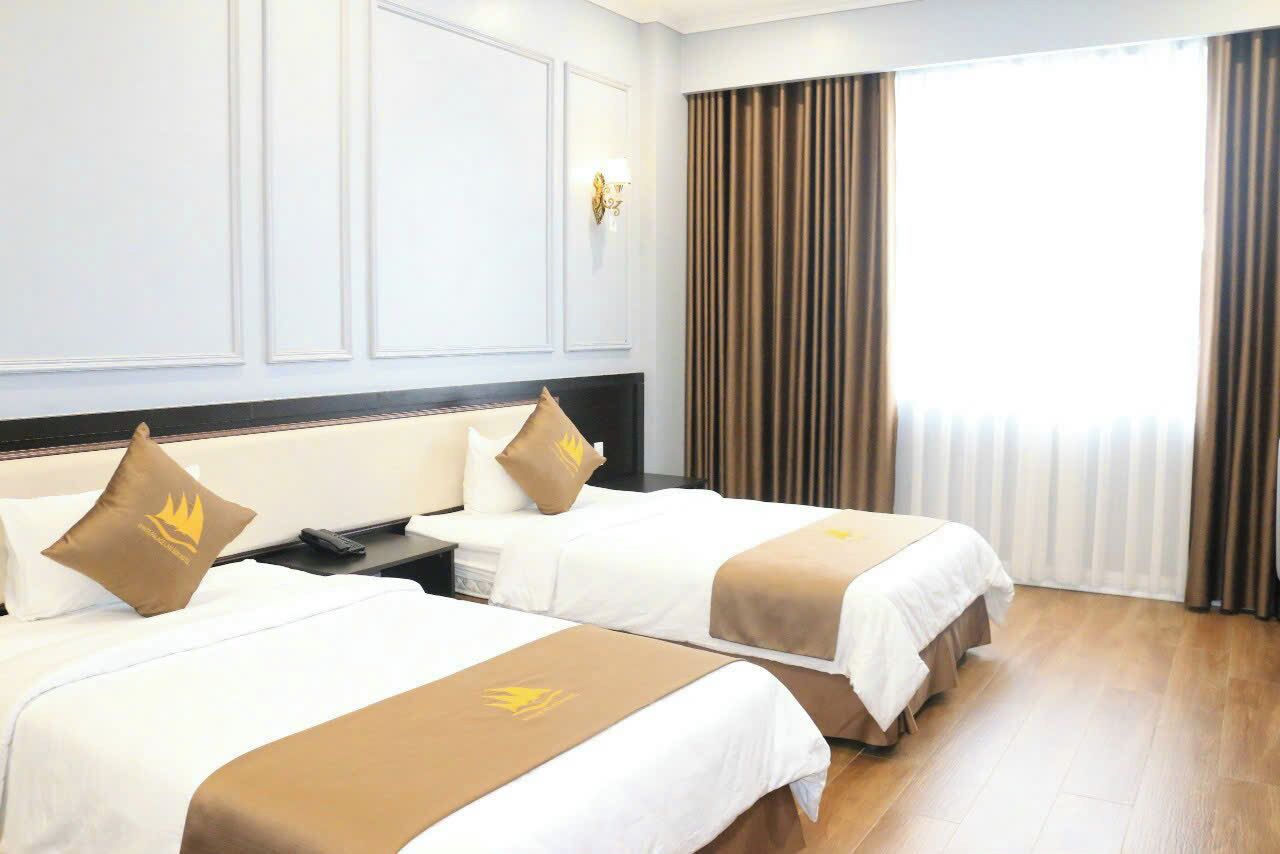 Una camera d'albergo con due letti, un comodino, una lampada e una finestra con tende.