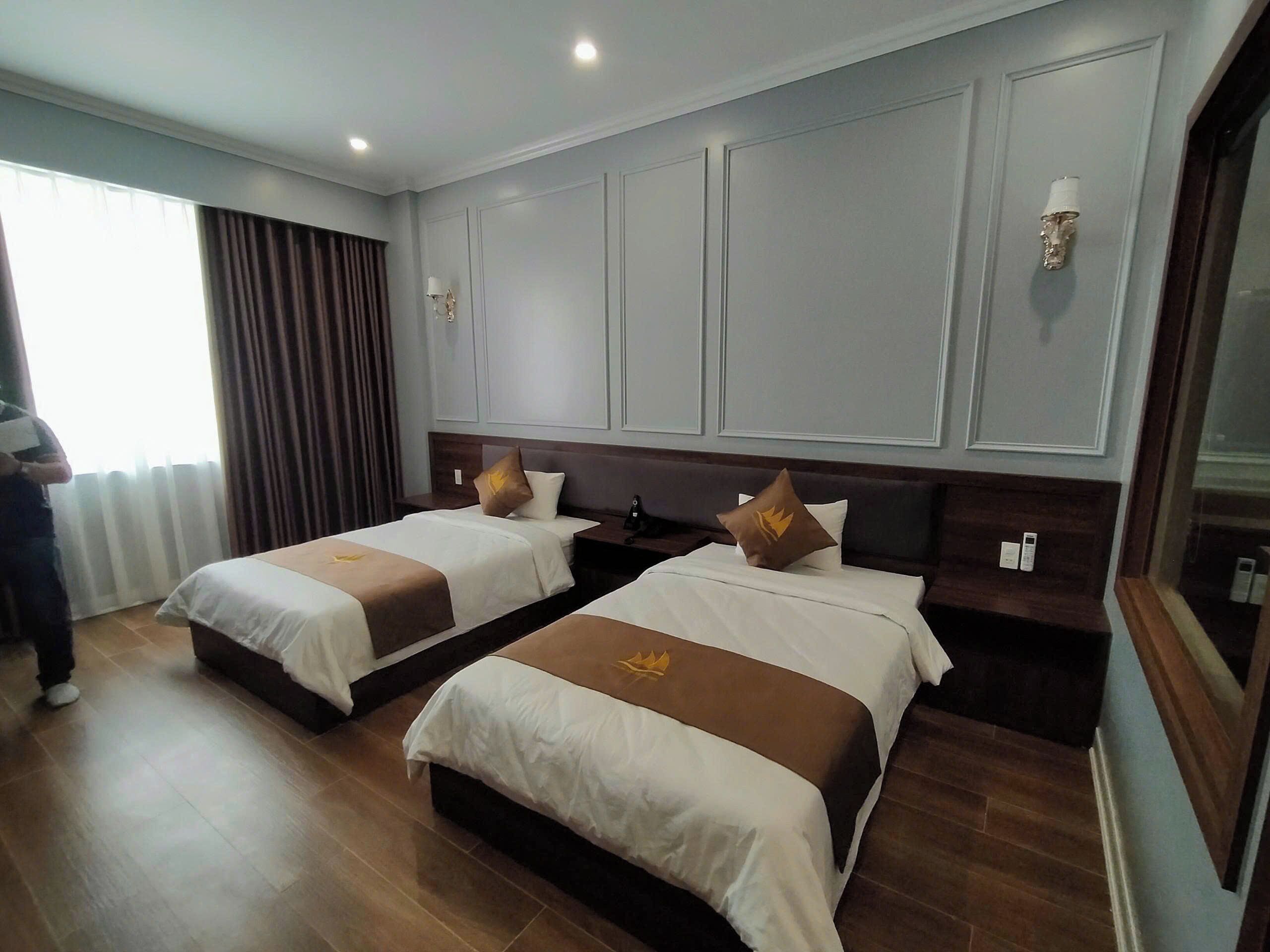 Habitación de hotel con dos camas, un ventanal con cortinas y suelo de madera.