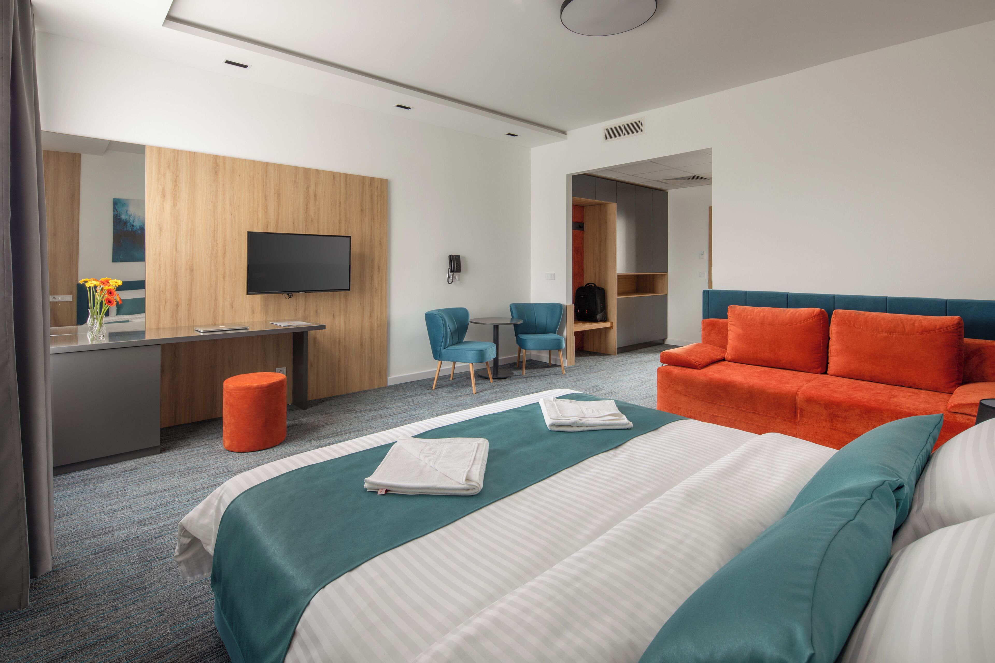 A hotel room with a bed, a desk, a TV, and a seating area.