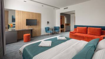 A hotel room with a bed, a desk, a TV, and a seating area.
