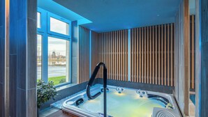 A modern spa room with a hot tub, wooden slats on the wall, and a view of a lake. - Sziget Hotel (Nyíregyháza)