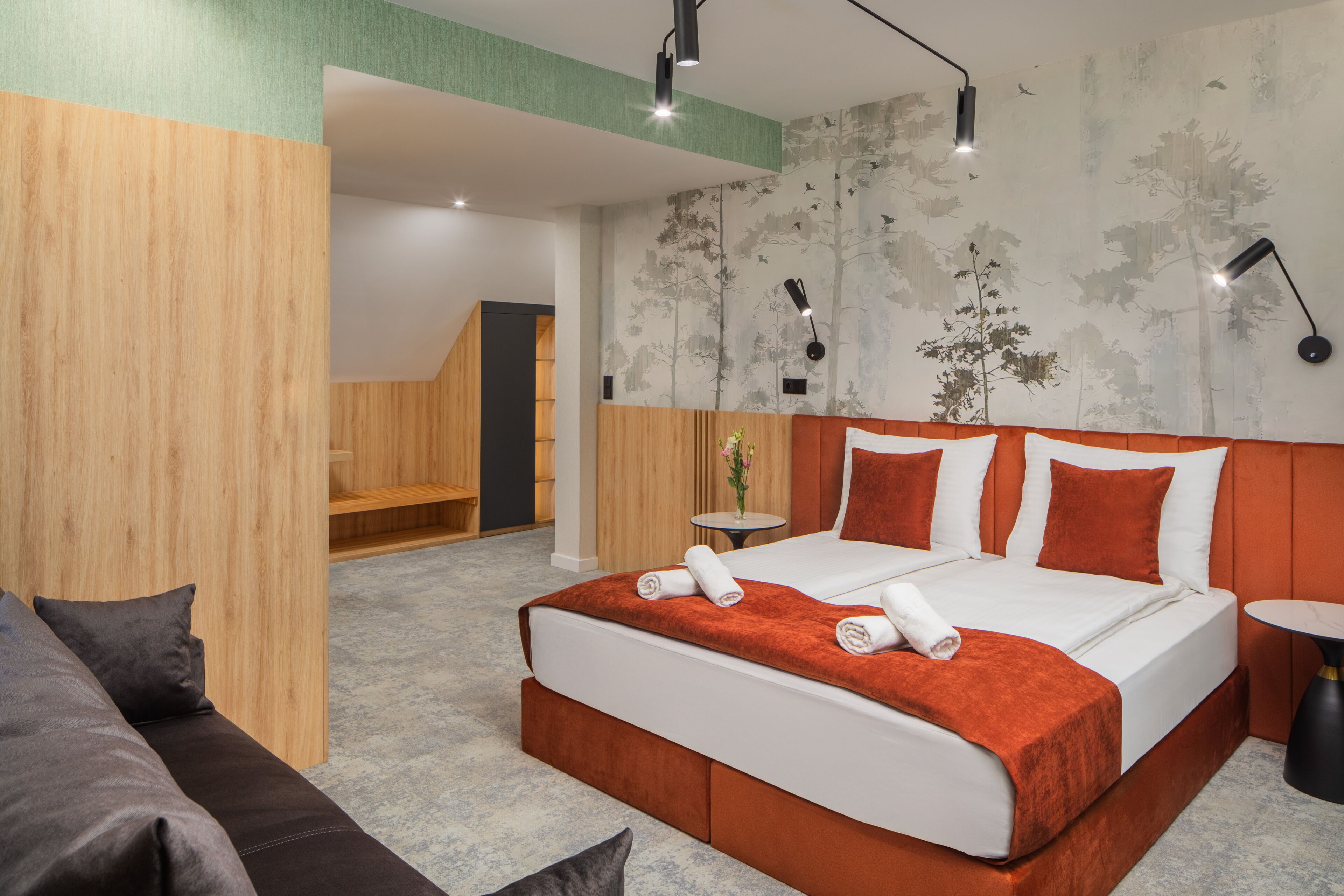 Une chambre d’hôtel moderne avec un grand lit, une petite table, un canapé et un mur recouvert d’un papier peint à motifs naturels.