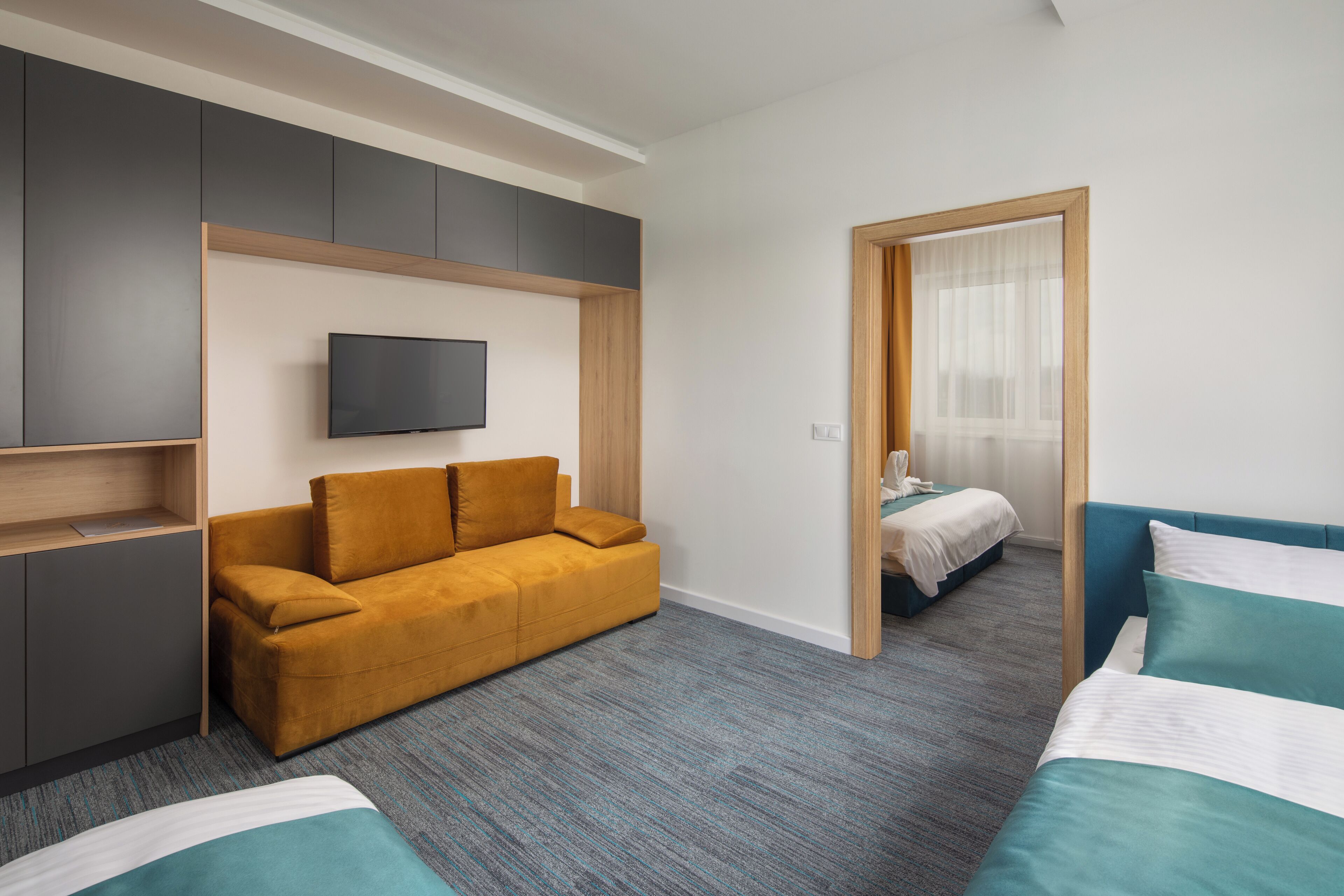 A modern hotel room with a sofa, two beds, a TV, and a wardrobe.