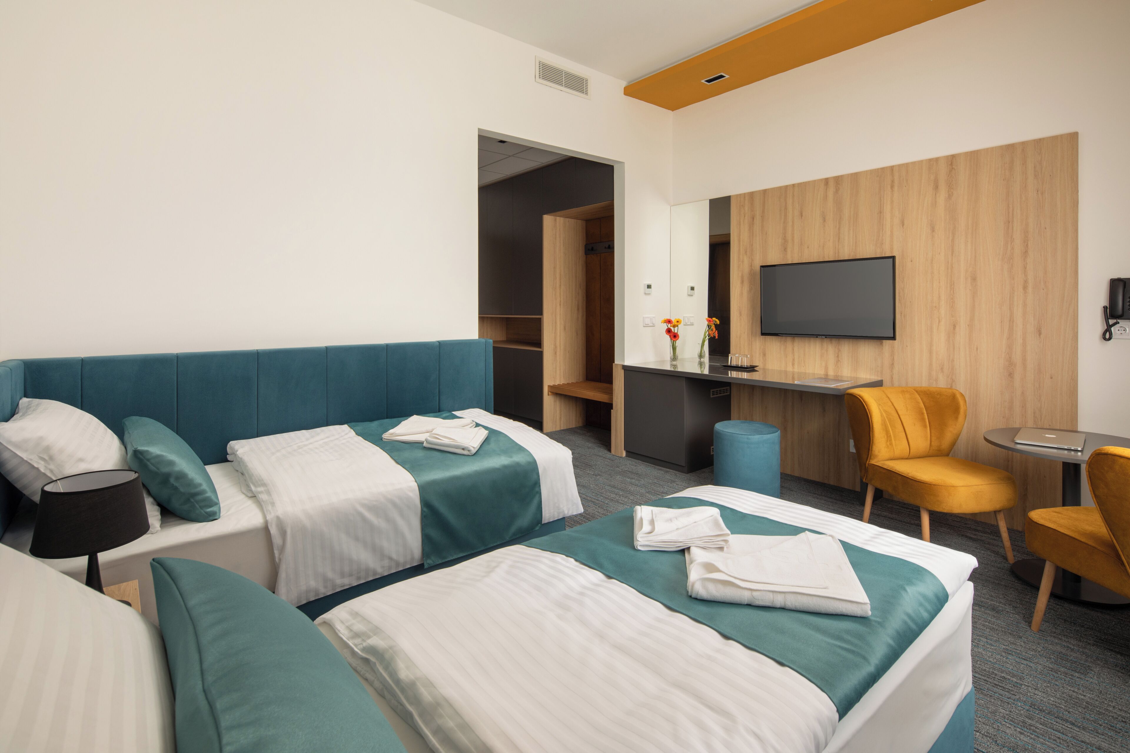 Una camera d'albergo con due letti, una scrivania, una sedia, una televisione e un armadio.