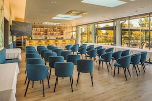 A spacious room with a bar area, multiple seating arrangements, and large windows offering a view of the outdoors. - Sziget Hotel (Nyíregyháza)