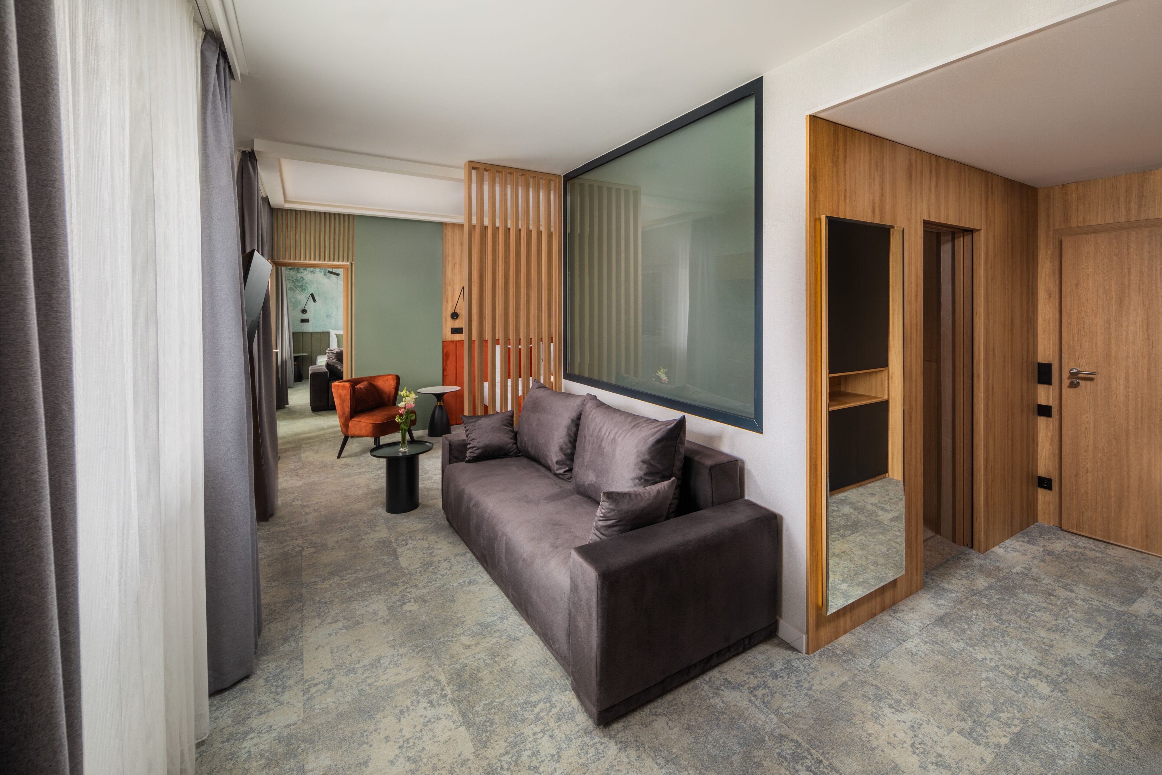 Una habitación de hotel moderna con un sofá gris, un armario de madera y un ventanal grande.