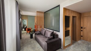 A modern hotel room with a grey sofa, a wooden wardrobe, and a large window. - Sziget Hotel (Nyíregyháza)