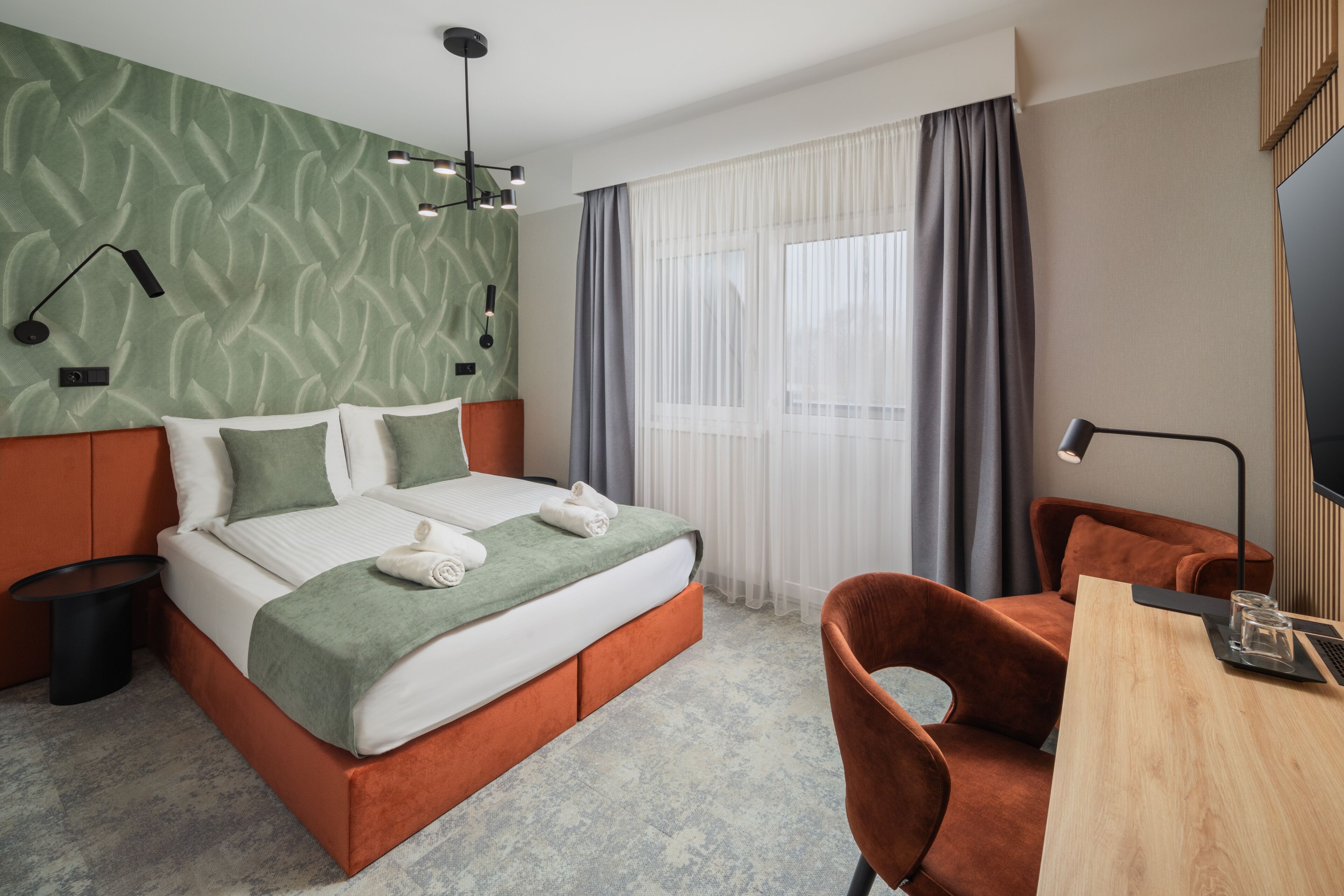 Habitación de hotel con una cama, una silla, un escritorio y un televisor.